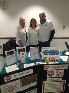 Three people standing in front of a table with information on it.