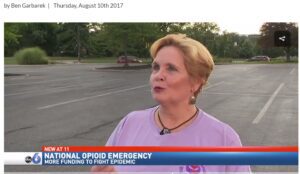 A woman in a purple shirt is talking on the news.