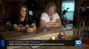 Two women sit at a counter in front of a television.