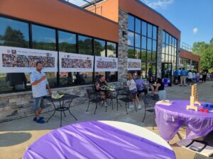 A group of people at an outdoor event with purple tablecloths.