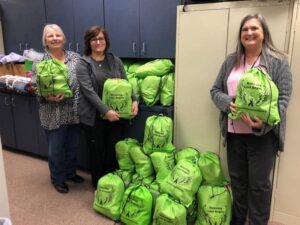 Three women standing in front of a room full of bags.