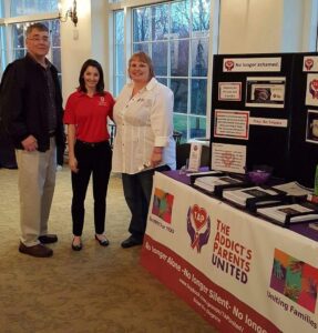 Three people standing in front of a table with a sign.