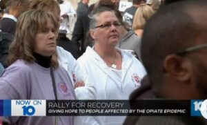 A group of people are standing in front of a rally for recovery.